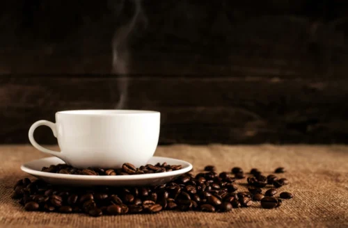 Steaming cup of coffee surrounded by coffee beans