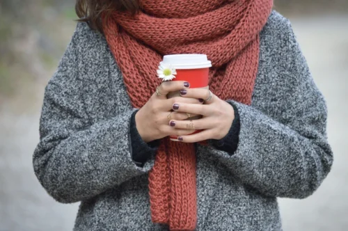 Person bundled up with a thick coat and scarf, holding a warm drink